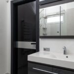Heated Floors - Creative design of bathroom with door between heated towel rail and washstand under rectangular mirror in light house