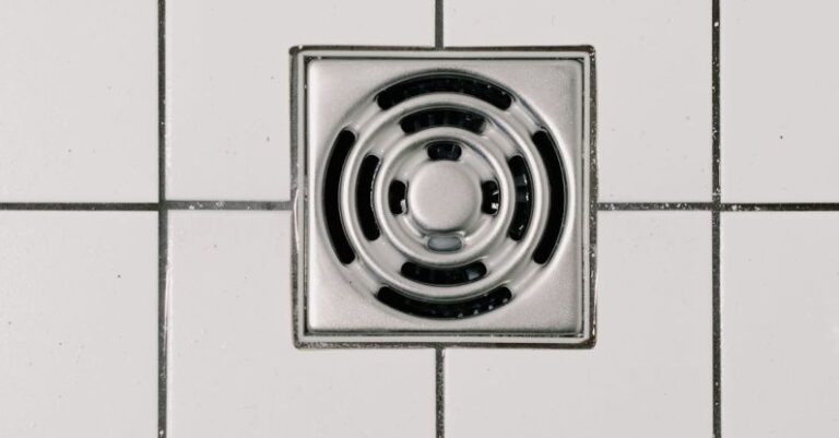 Unclogged Drain - Top view of white ceramic tile floor with stainless steel square shaped cover of drain in contemporary shower