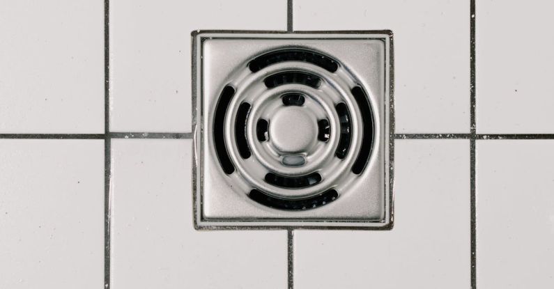 Unclogged Drain - Top view of white ceramic tile floor with stainless steel square shaped cover of drain in contemporary shower