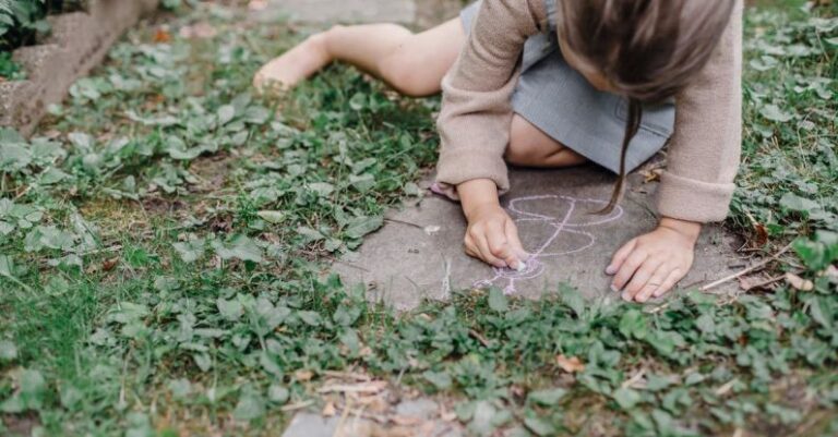 Chalk Paint - High angle of crop unrecognizable barefooted child painting on ground with colorful chalks while playing in green garden